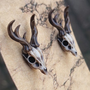 May include: A pair of brown and white deer skull earrings. The earrings are made of resin and have a realistic look.