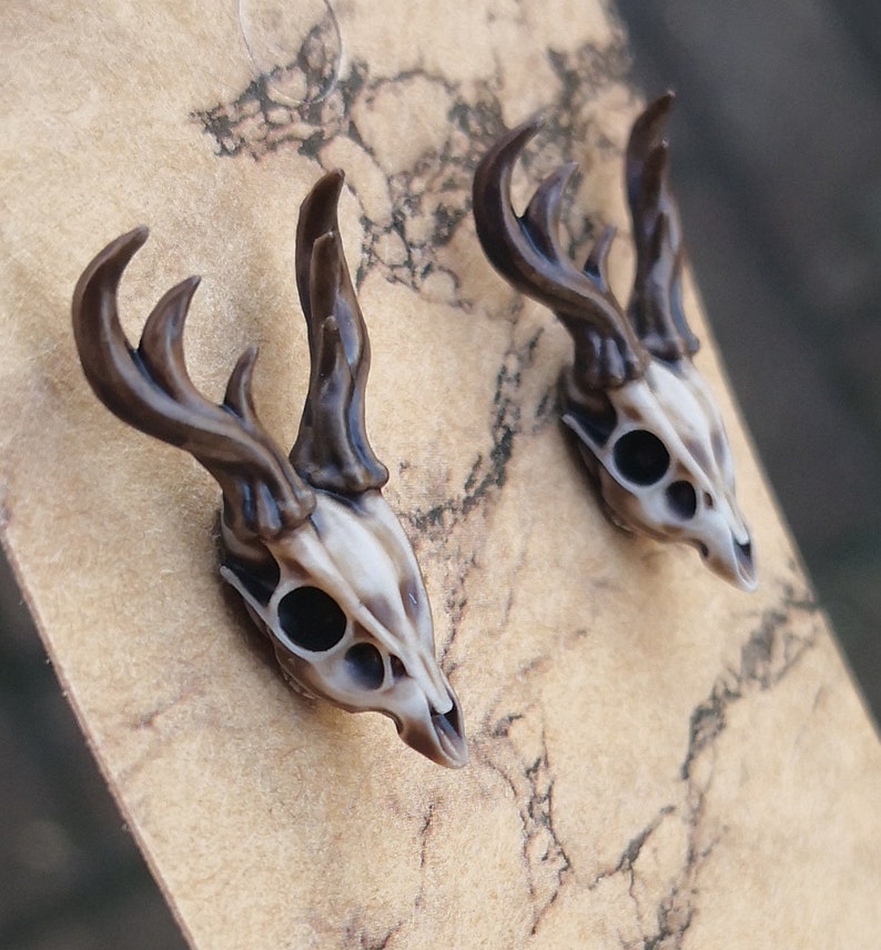 May include: A pair of brown and white deer skull earrings. The earrings are made of resin and have a realistic look.