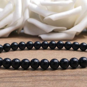 May include: A black beaded bracelet made of round, smooth stones. The bracelet is lying on a wooden surface.