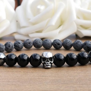 May include: A black and grey beaded bracelet with a silver skull charm. The bracelet is made with lava rock and onyx beads.