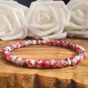 May include: A circular beaded bracelet featuring small, round beads with a white base color and a vibrant red marbled or splatter pattern. The beads are uniform in size and arranged in a continuous loop, creating a striking contrast between the white and red.