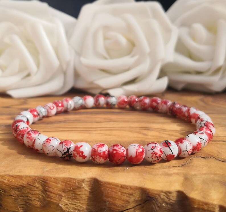 May include: A circular beaded bracelet featuring small, round beads with a white base color and a vibrant red marbled or splatter pattern. The beads are uniform in size and arranged in a continuous loop, creating a striking contrast between the white and red.