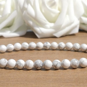 May include: A white howlite beaded bracelet with a simple design. The bracelet is made of small, round beads that are strung together on a clear elastic cord.