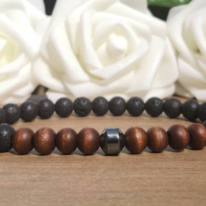 May include: A bracelet with black lava rock beads, brown wooden beads, and a dark grey faceted bead. The bracelet is elasticated. The background features white roses. The beads are approximately 8mm in diameter.