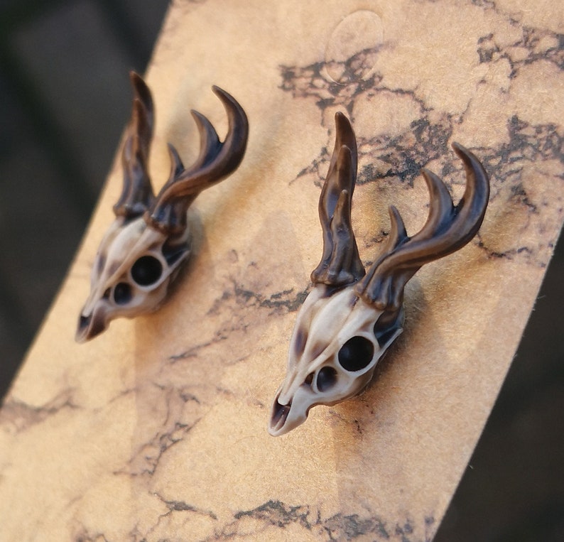 May include: A pair of deer skull earrings with brown antlers. The earrings are made of a light brown resin and have a realistic look.