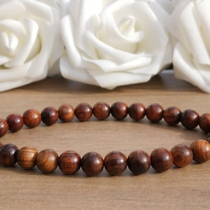 May include: A brown wooden beaded bracelet with a smooth, polished finish. The bracelet is made of round beads and is laid out on a wooden surface.