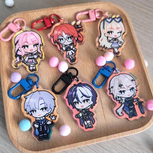 Könnte beinhalten: Sechs bunte Anime-Charakter-Schlüsselanhänger mit klaren Acryl-Rückseiten. Die Schlüsselanhänger zeigen Charaktere mit verschiedenen Haarfarben, Outfits und Gesichtsausdrücken. Jeder Schlüsselanhänger hat einen Metallring zum Anbringen an einer Tasche oder einem anderen Gegenstand.
