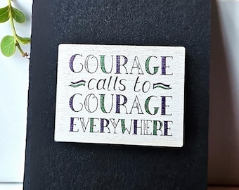 Broche de madera con la frase inspiradora de las sufragistas: «El coraje llama al coraje en todas partes».