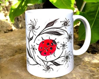 Taza Mariquita: Preciosa taza con linograbado de una mariquita entre flores. Representa buena suerte, nuevos comienzos y cambios positivos. Apta para lavavajillas.
