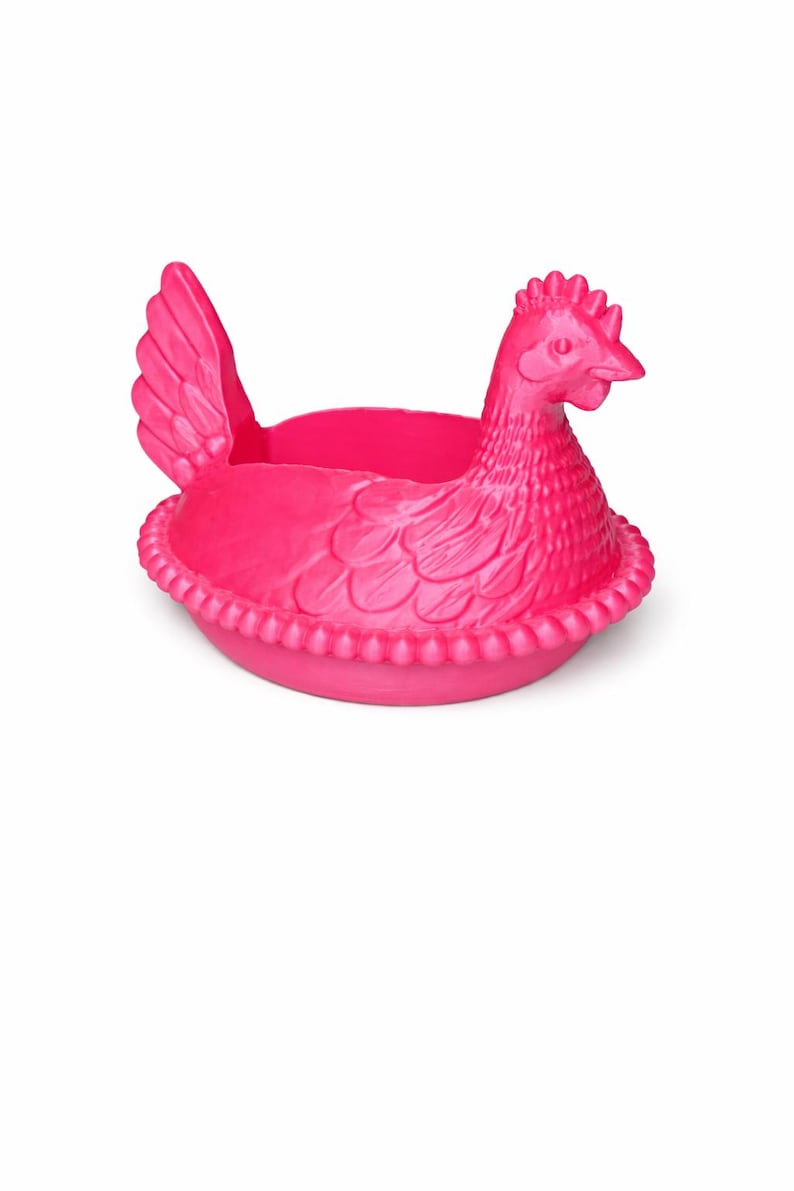 May include: A bright pink hen-shaped planter. The planter features a detailed hen with a textured body, a comb, and a beak. The base of the planter has a decorative beaded edge. The hen's wings are visible on the side.