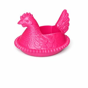 May include: A bright pink chicken-shaped container. The hen is sitting in a nest-like base. The container has a detailed design, including a comb, beak, and wing. The container is made of a solid material.