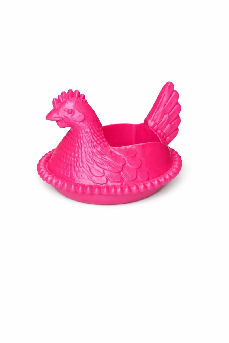 May include: A bright pink chicken-shaped container. The hen is sitting in a nest-like base. The container has a detailed design, including a comb, beak, and wing. The container is made of a solid material.