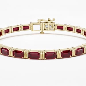 May include: A gold bracelet with rectangular, deep red gemstones. The bracelet has a secure clasp and is set in a gold band. The gemstones are evenly spaced around the bracelet, creating a continuous pattern. The jewellery is displayed on a white background.
