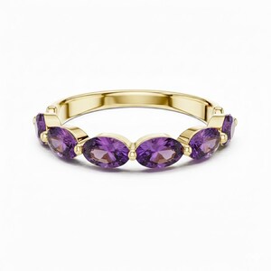 Puede incluir: Un anillo de oro con una banda engastada con piedras preciosas moradas de corte ovalado. Las piedras están dispuestas en una fila, creando una línea continua de color. El anillo tiene una superficie pulida y las piedras son de un morado intenso.