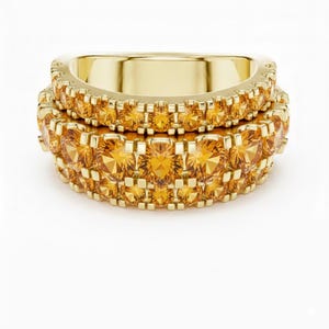 Puede incluir: Dos anillos dorados, cada uno adornado con una banda de pequeñas gemas redondas de color amarillo-naranja. Los anillos están apilados, mostrando el patrón repetitivo de las gemas. Superficie pulida y reflectante.