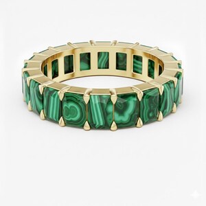 May include: A gold ring featuring rectangular malachite stones. The ring's band is gold, and the malachite stones are a vibrant green with darker green veining. The ring is set against a white background.