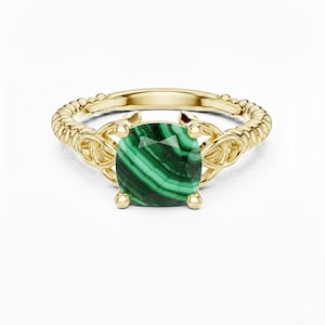 May include: A gold ring with a square malachite gemstone. The ring has a twisted band and decorative filigree. The malachite stone is a vibrant green with darker green veining.