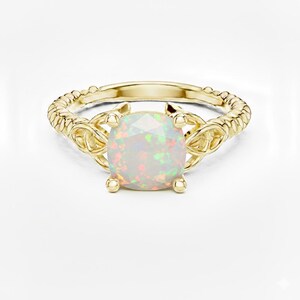 Könnte beinhalten: Ein goldener Ring mit einem großen, quadratischen, schillernden Opal-Edelstein. Das Band hat ein gedrehtes Seilmuster, und der Edelstein wird von vier Krappen gehalten. Der Ring ist vor einem weißen Hintergrund platziert.