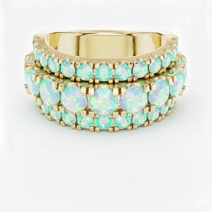 May include: Two gold rings stacked together, each adorned with rows of iridescent opal gemstones. The opals display a range of colours, including pale blues and greens, set against the warm gold band. The rings are displayed on a white background.
