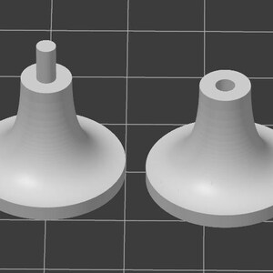 以下が含まれることがあります： 2つのライトグレーの3Dレンダリングされたキャビネットノブ。1つのノブは上部から伸びる円筒形のポストがあり、もう1つは穴があります。どちらのノブも丸みを帯びたベースと円錐形のボディを備えています。背景は濃い灰色のグリッドです。