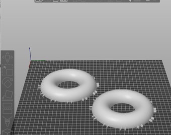 May include: Two white donut-shaped objects with a hole in the center. The objects are on a gray grid surface.