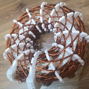 Puede incluir: Primer plano de una bobina de alambre de cobre envuelta alrededor de una forma de plástico blanco. La bobina tiene la forma de una rosquilla, y la forma de plástico es visible a través del alambre.