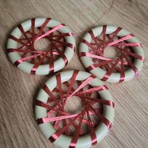 May include: Three beige circular coils with red wire wrapped around them. The coils are arranged in a triangular pattern on a wooden surface.