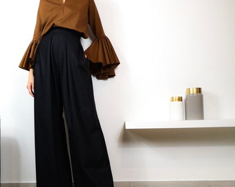 May include: A woman is wearing a brown blouse with large bell sleeves and black wide-leg pants.
