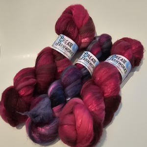 Puede incluir: Tres ovillos de hilo teñido a mano en tonos de rosa, morado y negro. El hilo está etiquetado con "Create Yarnworks" y tiene una dirección de sitio web.