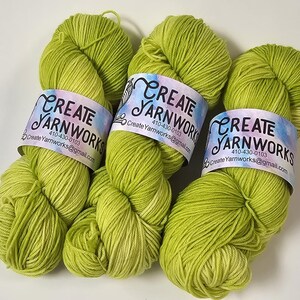 May include: Three skeins of green yarn with a gradient from a darker green to a lighter green. Each skein has a label that reads "CREATE YARNWORKS" with a phone number and email address.