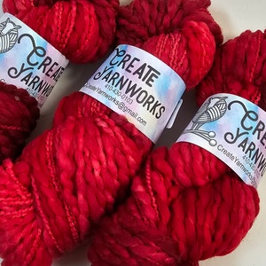 Pode incluir: Tr&ecirc;s novelos de fio vermelho e rosa com um r&oacute;tulo branco que diz "Create Yarnworks 410-430-0103 CreateYarnworks@gmail.com"