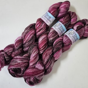 Puede incluir: Dos ovillos de hilo teñido a mano en tonos de rosa, blanco y negro. El hilo está etiquetado con "Create Yarnworks".