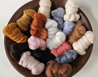 May include: A wooden bowl filled with various colors of wool roving. The roving is arranged in small, fluffy bundles. Colors include shades of gold, orange, pink, black, white, gray, and brown. The bowl is a dark brown color.