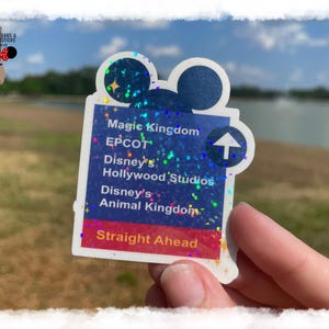 Puede incluir: Una pegatina azul y rosa brillante con una cabeza de Mickey Mouse y una flecha apuntando hacia arriba. La pegatina enumera los nombres de los diferentes parques de Walt Disney World: Magic Kingdom, EPCOT, Disney's Hollywood Studios y Disney's Animal Kingdom. El texto "Straight Ahead" está en la parte inferior de la pegatina.