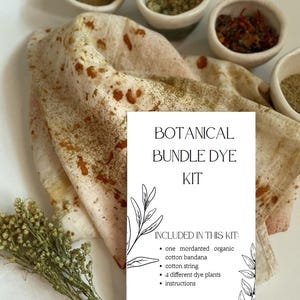 May include: A botanical bundle dye kit featuring a white card with black text reading BOTANICAL BUNDLE DYE KIT and a list of contents. The kit includes a mordanted organic cotton bandana with rust-colored spots, four small bowls of dye plants, and dried herbs.