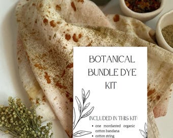 May include: A botanical bundle dye kit featuring a white card with black text reading BOTANICAL BUNDLE DYE KIT and a list of contents. The kit includes a mordanted organic cotton bandana with rust-colored spots, four small bowls of dye plants, and dried herbs.