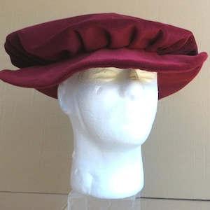 May include: A burgundy velvet hat with a flat, round crown and a wide brim. The hat is sitting on a white mannequin head.