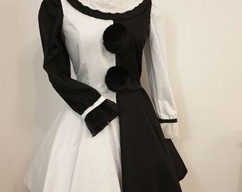 Puede incluir: Un vestido blanco y negro con cuello de encaje y pompones negros. El vestido tiene un corpiño ajustado y una falda completa.
