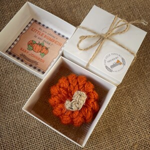 May include: A small, orange crocheted pumpkin in a white gift box. The box is tied with twine and has a sticker that says "Farm Fresh Pumpkins Picked Fresh Daily".