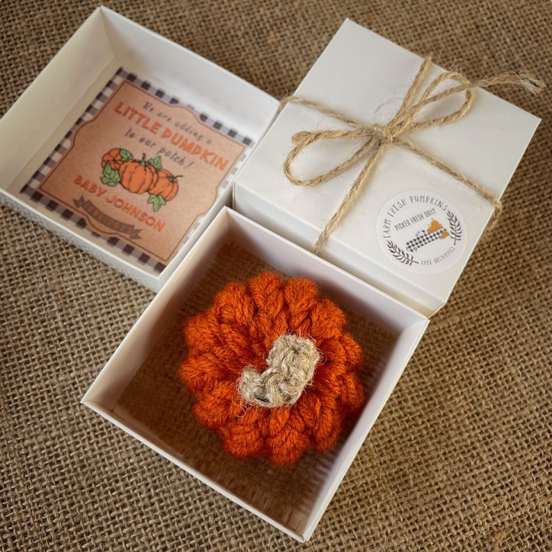 May include: A small, orange crocheted pumpkin in a white gift box. The box is tied with twine and has a sticker that says "Farm Fresh Pumpkins Picked Fresh Daily".