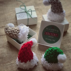 Pu&ograve; includere: Quattro piccoli cappelli di Babbo Natale a maglia in rosso, verde, beige e grigio con pon pon bianchi. I cappelli sono in piccole scatole con il testo "Siamo entusiasti di annunciare che un piccolo regalo &egrave; in arrivo! Stiamo aspettando un bambino!"