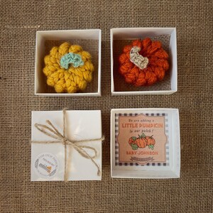 May include: Three white gift boxes with lids. Two boxes contain crocheted pumpkins, one orange and one yellow. The third box has a label that reads "We are adding a LITTLE PUMPKIN to our patch! BABY JOHNSON".