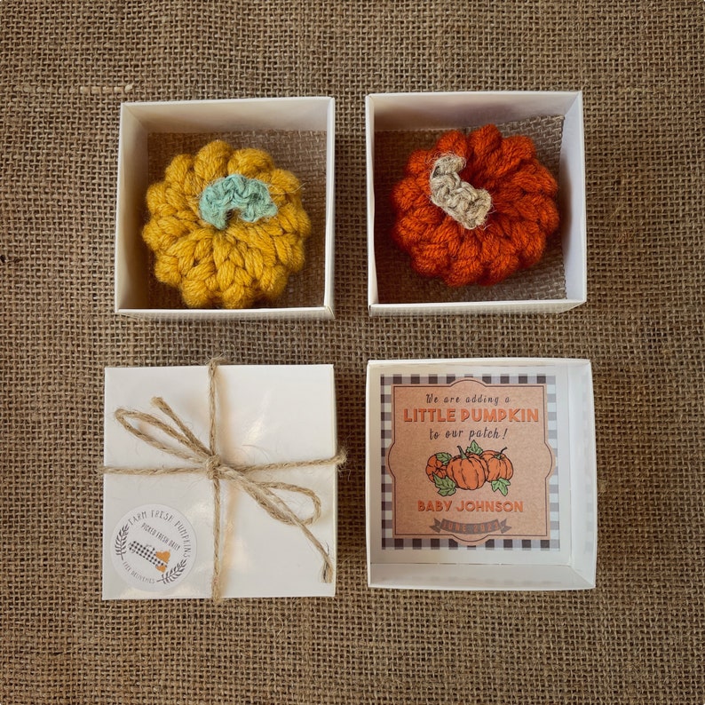 May include: Three white gift boxes with lids. Two boxes contain crocheted pumpkins, one orange and one yellow. The third box has a label that reads "We are adding a LITTLE PUMPKIN to our patch! BABY JOHNSON".