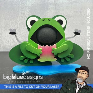 Peut inclure: Une grenouille verte tenant une fleur rose, assise sur un nénuphar bleu. La grenouille a une grande bouche et des yeux noirs. La grenouille est un fichier de conception découpé au laser. Le texte "Laser bigbluedesigns LASER-READY CREATIVITY THIS IS A FILE TO CUT ON YOUR LASER" est en bas de l'image.