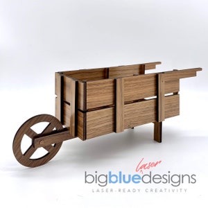 May include: A wooden wheelbarrow with a single wheel and a rectangular box. The wheelbarrow is made of light brown wood with a wood grain pattern. The wheelbarrow is a decorative item and is not intended for use.