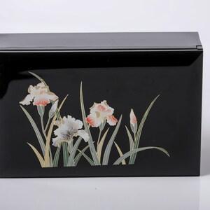May include: A black rectangular box with a glossy finish. The front of the box is decorated with a floral design featuring irises in shades of white, peach, and green. The box has a hinged lid.