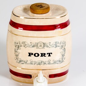 May include: Cream-colored ceramic barrel-shaped container with red bands and gold trim. The word "PORT" is displayed in bold black letters on the front. A wooden stopper sits on top, and a white spigot is on the front.
