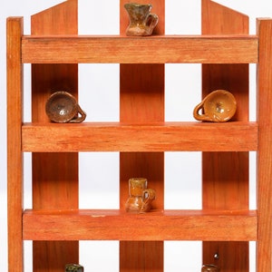 May include: A wooden shelf unit with four shelves, each displaying a small, brown, ceramic mug. The shelf unit is painted a reddish-brown color and has a rustic, farmhouse style.