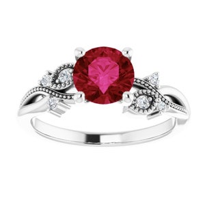 May include: A silver ring featuring a large, round, deep red gemstone as the centerpiece. The ring has a floral design with small, clear accent stones and delicate detailing on the band, creating an elegant and romantic look. The ring is a piece of jewelry.