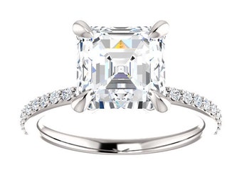 May include: A silver engagement ring featuring a square-shaped, clear, centre stone and a band of smaller, clear stones.